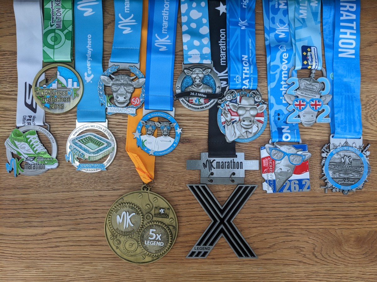 A collection of MK Marathon finisher medals from multiple years laid out on a wooden surface, showing the variety of designs across different editions.